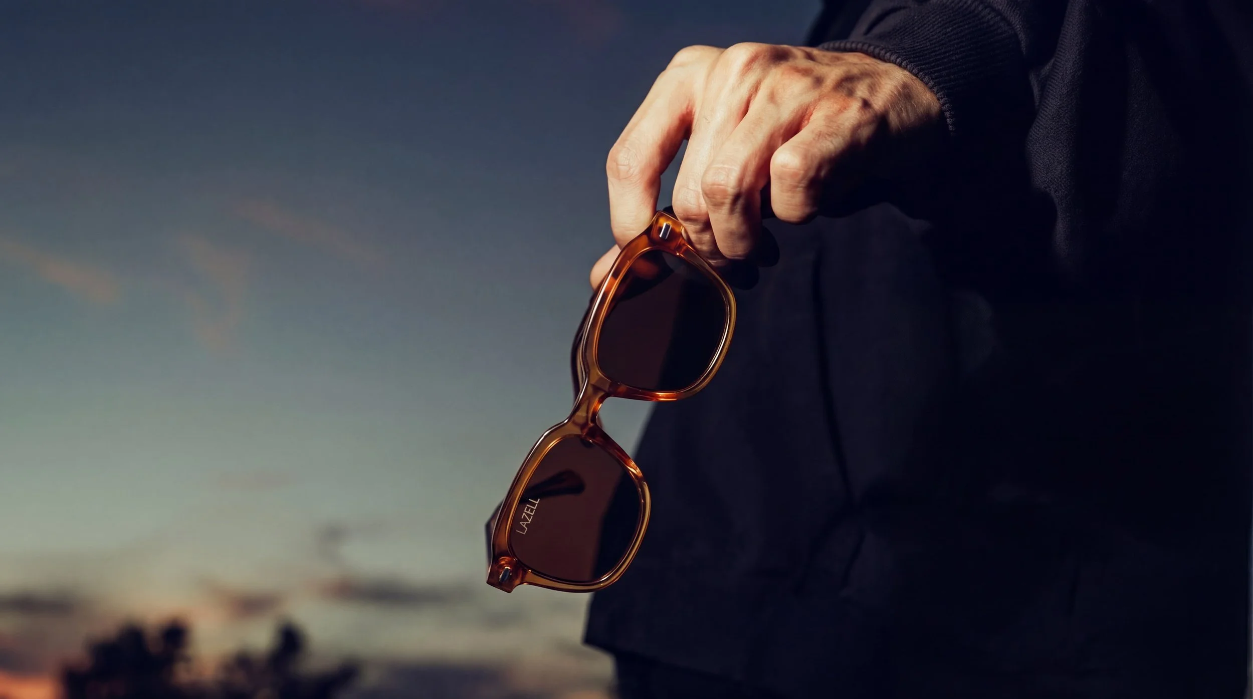 Hands holding Lazell sunglasses in the evening light